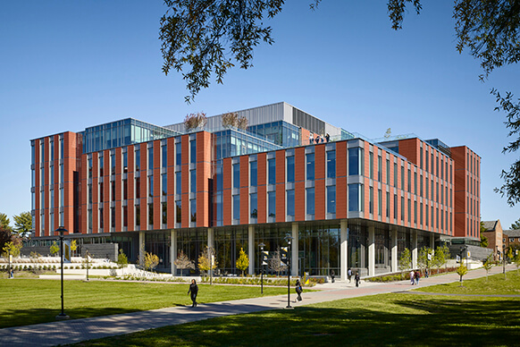 Modern university building with red brick facade and large glass windows on a sunny day.