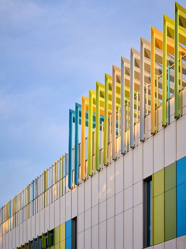 Colorful building facade with unique slatted roof design and large panels in green, blue, and yellow against a clear sky.