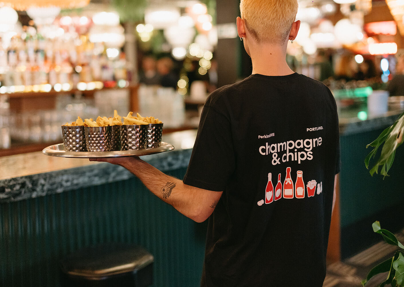 Server carrying fries on a tray at a lively bar scene.