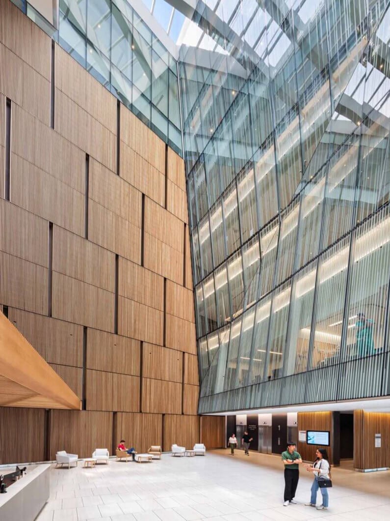 Modern atrium with wood and glass design, featuring seating area, high ceilings, and natural light.